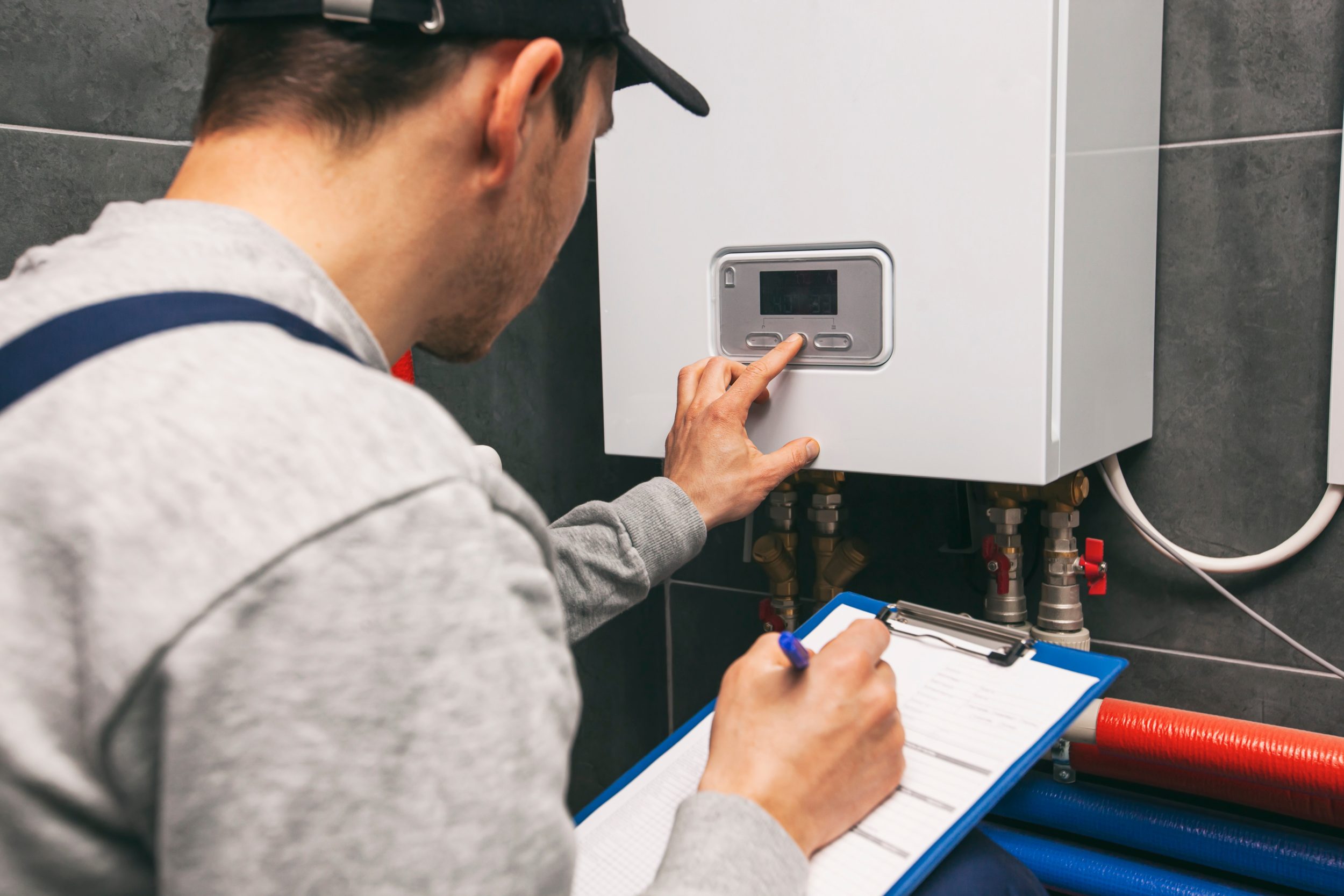 Technician servicing a boiler while holding a clipboard and pen.