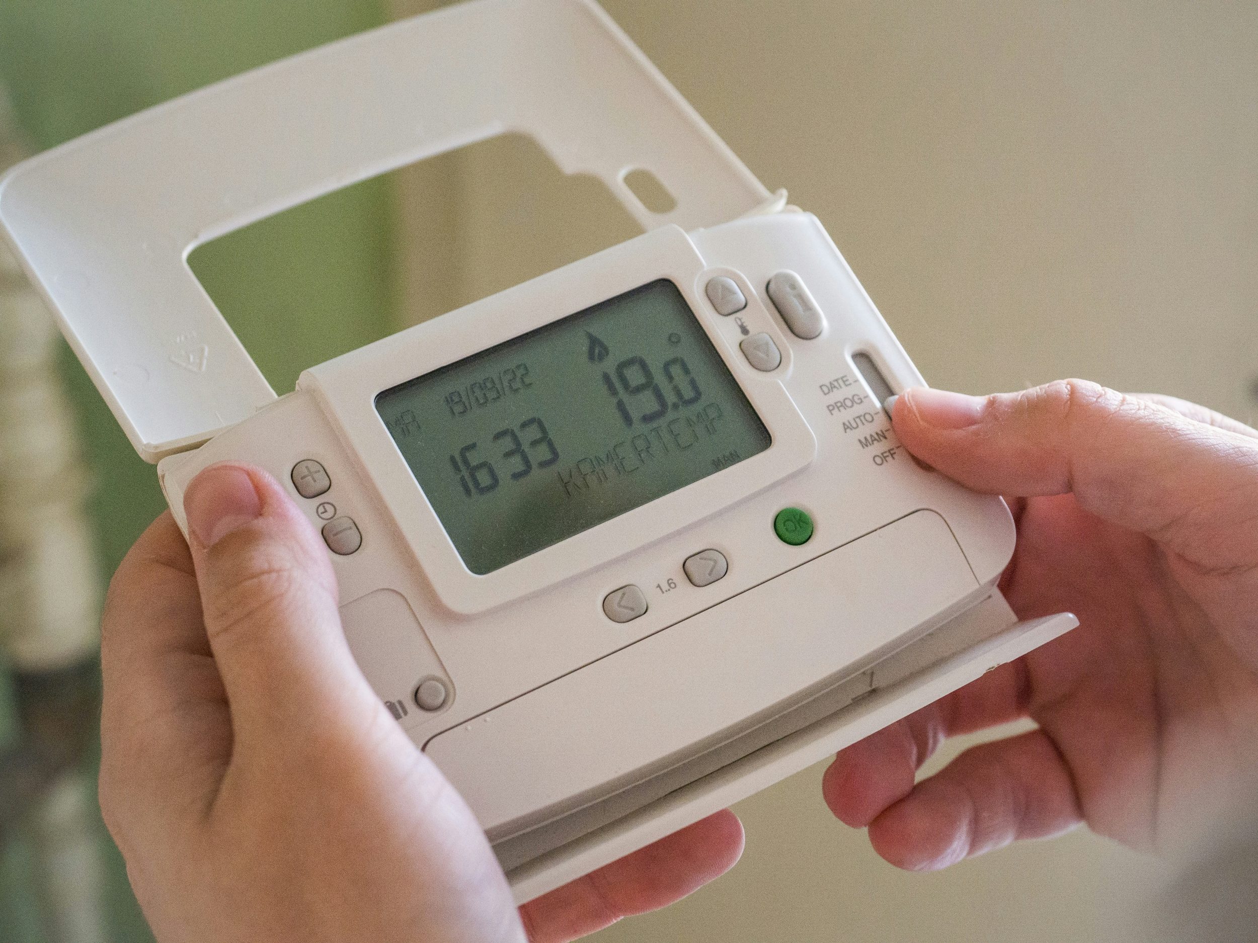 Person holding an electric thermostat in a home.